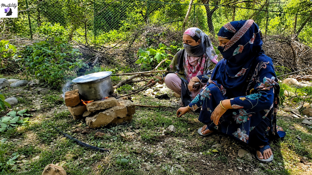 Two women from an affected family prepare food over a makeshift fire near the remains of their demolished home
